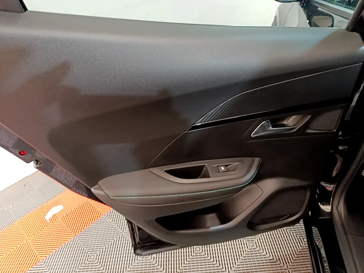 Vue rapprochée de la porte arrière droite noire du Peugeot 2008 PureTech 130 avec garniture carbone et surpiqûres bleues.