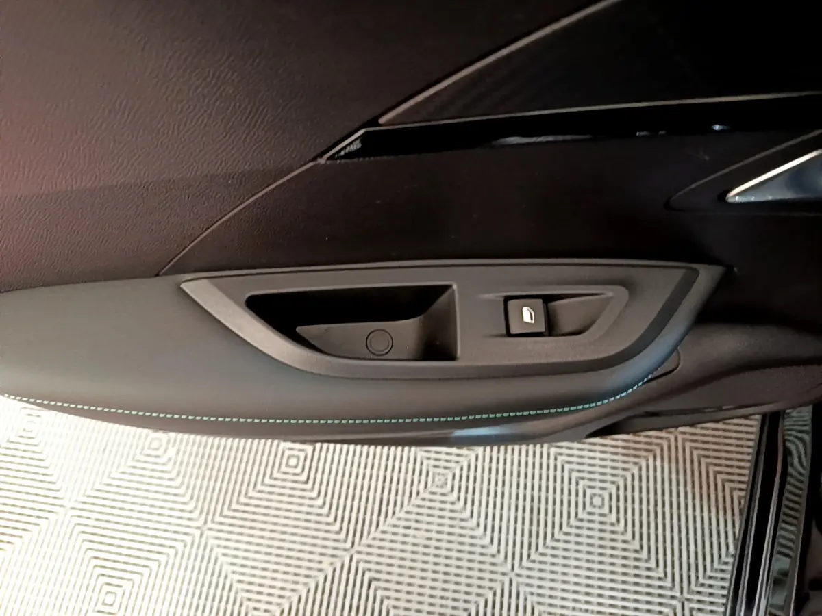 Gros plan sur la poignée intérieure côté gauche de la porte d'une Peugeot 2008 noire avec couture bleue décorative.