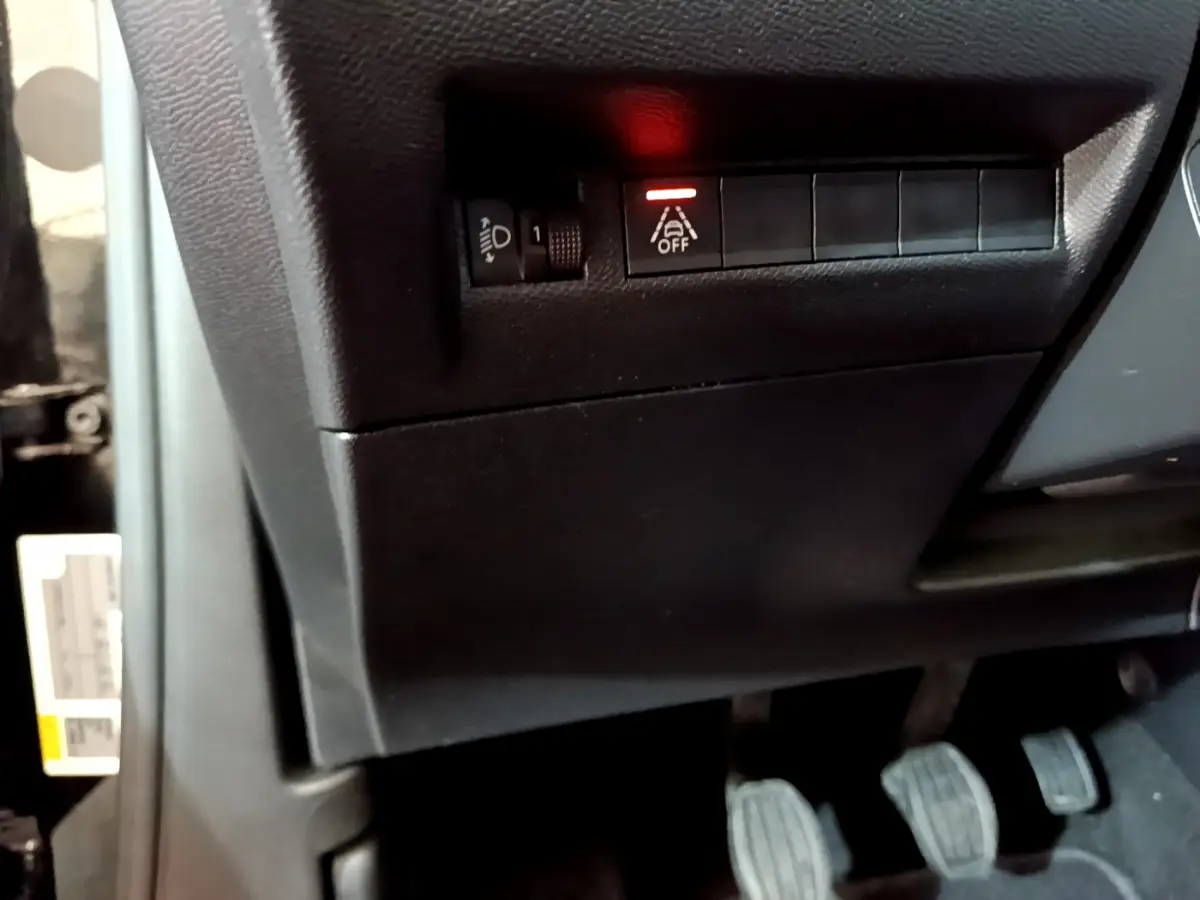 Gros plan sur les commandes sous le tableau de bord côté gauche du Peugeot 2008 noir, avec pédales et bouton d'aide à la conduite allumé.