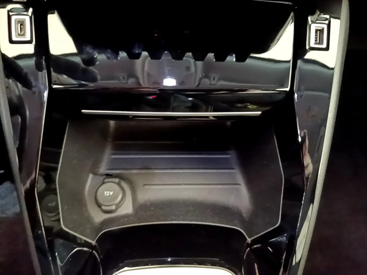 Gros plan sur la console centrale noire du Peugeot 2008, montrant la prise 12V et les finitions brillantes autour.