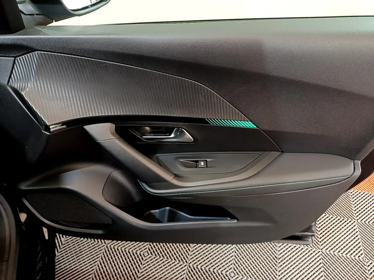 Vue intérieure côté gauche de la porte noire du Peugeot 2008 PureTech 130 avec insert carbone et surpiqûres bleues.