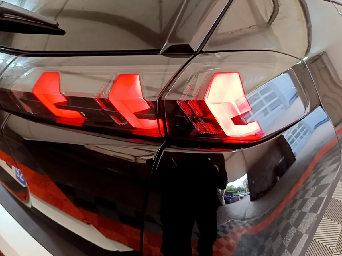 Gros plan sur le feu arrière droit rouge vif d'un Peugeot 2008 noir brillant, reflet d'un garage visible.