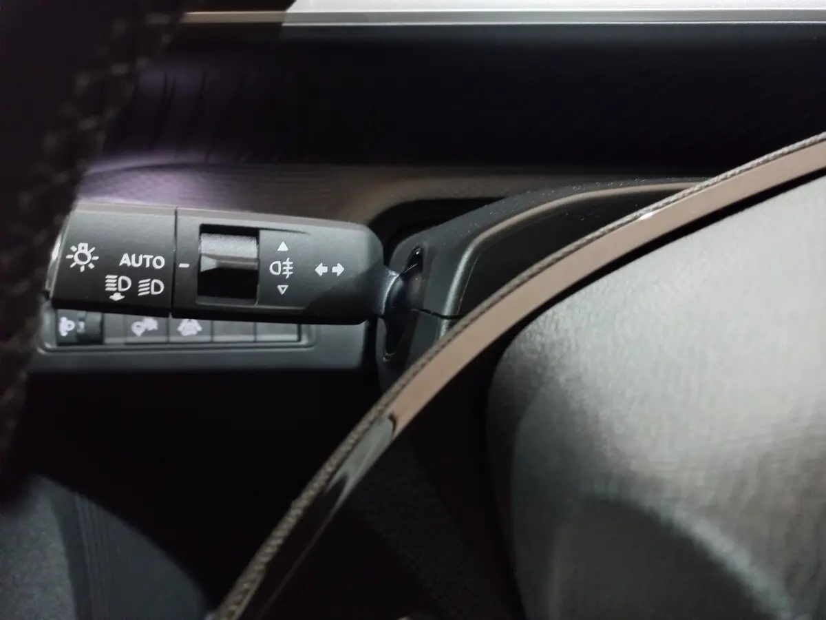 Gros plan sur la commande des phares et clignotants à gauche du volant dans une Citroën C3 gris foncé 2025 hybride.