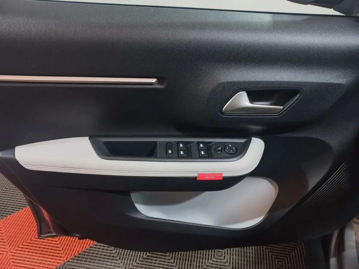 Vue rapprochée de la porte côté conducteur de la Citroën C3 hybride 2025, avec garniture noire et blanche et commandes électriques.