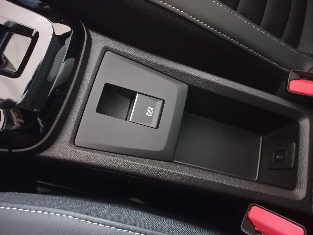 Gros plan sur la console centrale noire de la Citroën C3 hybride 2025, avec frein à main électrique et port USB visible.