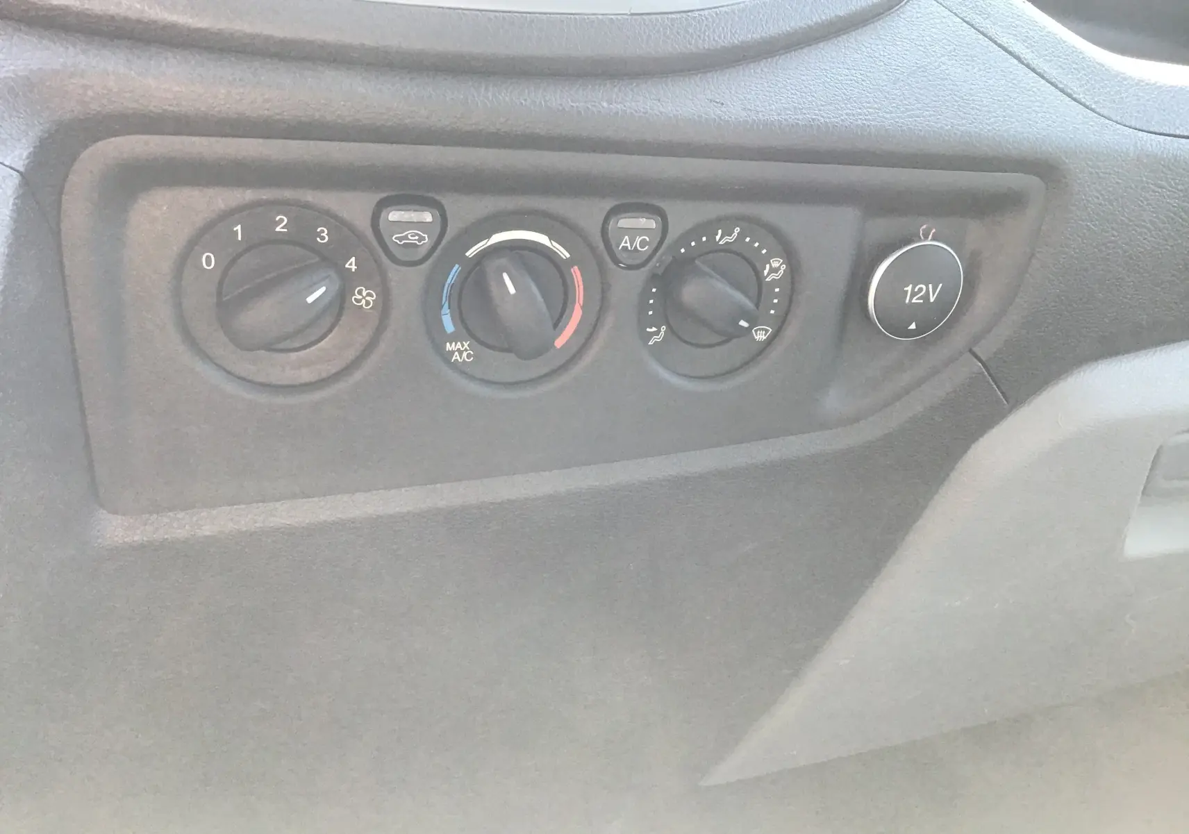 Panneau de commande de climatisation avec boutons rotatifs et prise 12V dans l'habitacle du Ford Transit blanc.