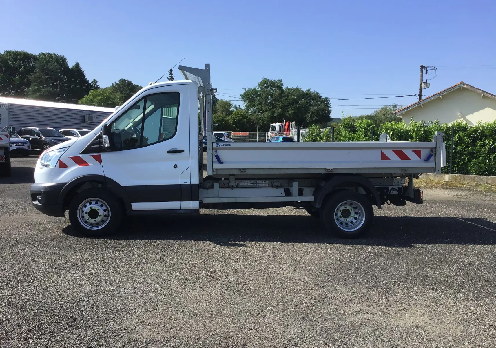 Ford Transit Chassis Cabine blanc vu de profil côté gauche avec benne arrière et bandes rouges réfléchissantes.