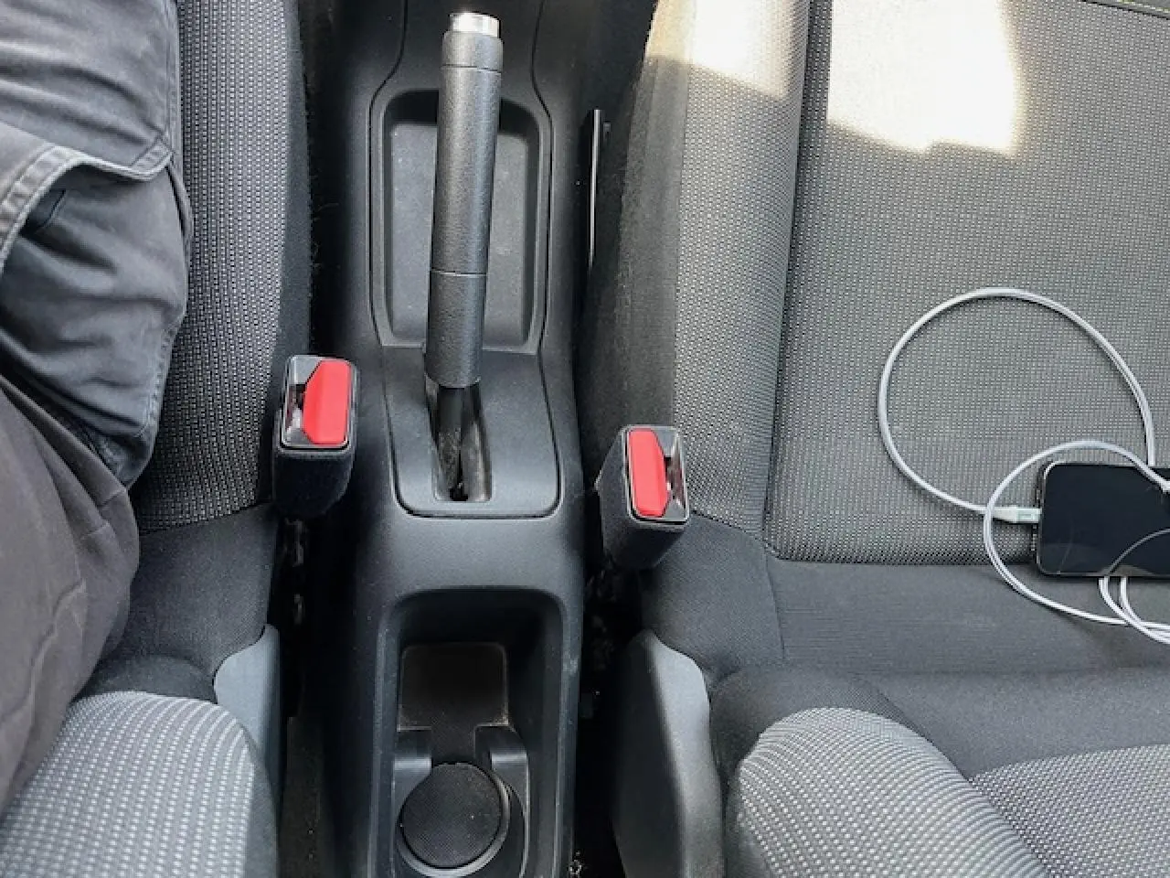 Vue plongeante sur la console centrale et les sièges noirs d'une Citroën C3 2023 avec frein à main manuel et smartphone connecté.