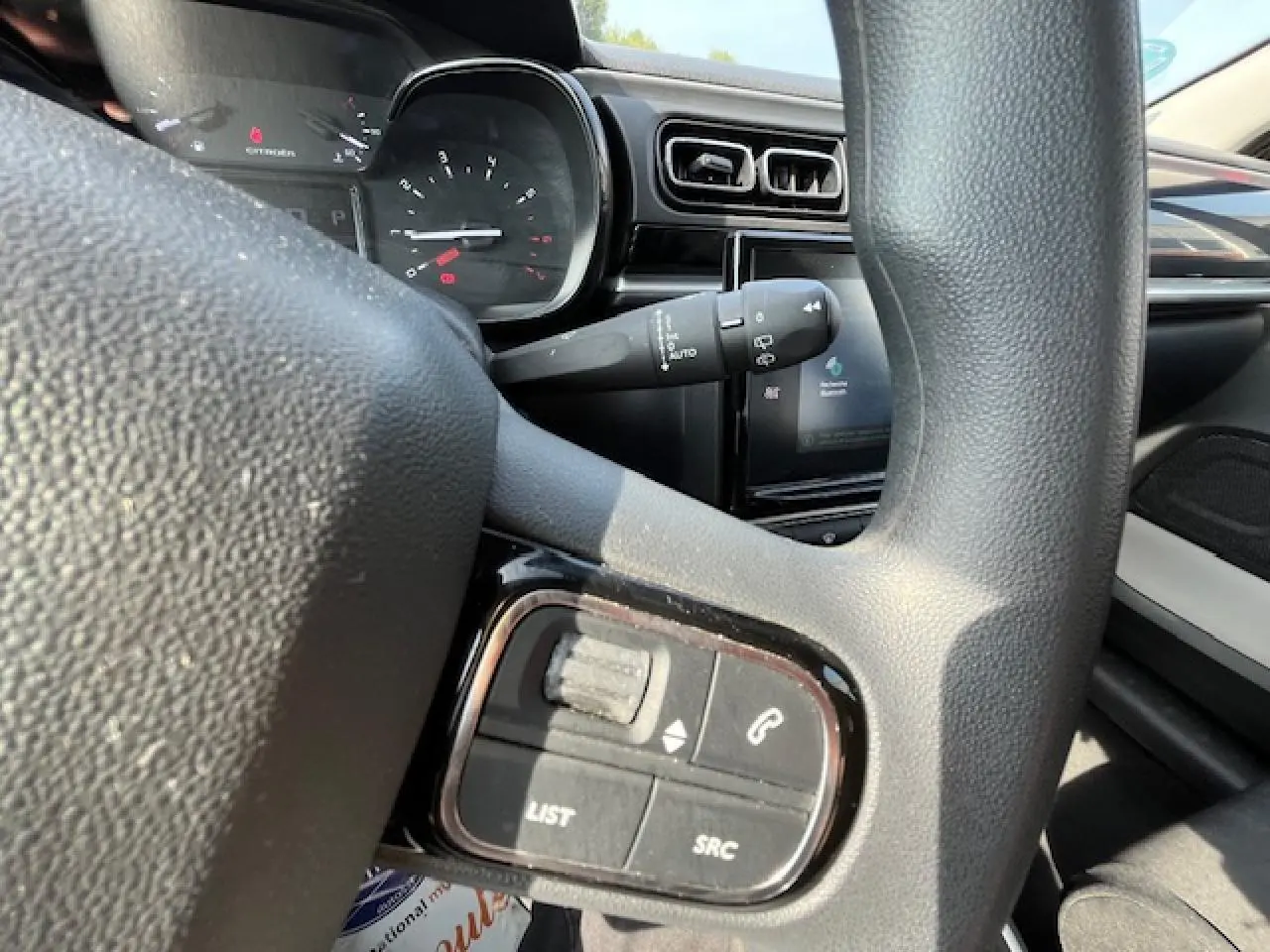 Gros plan sur les commandes audio au volant d'une Citroën C3 noire de 2023, avec tableau de bord et écran tactile en arrière-plan.