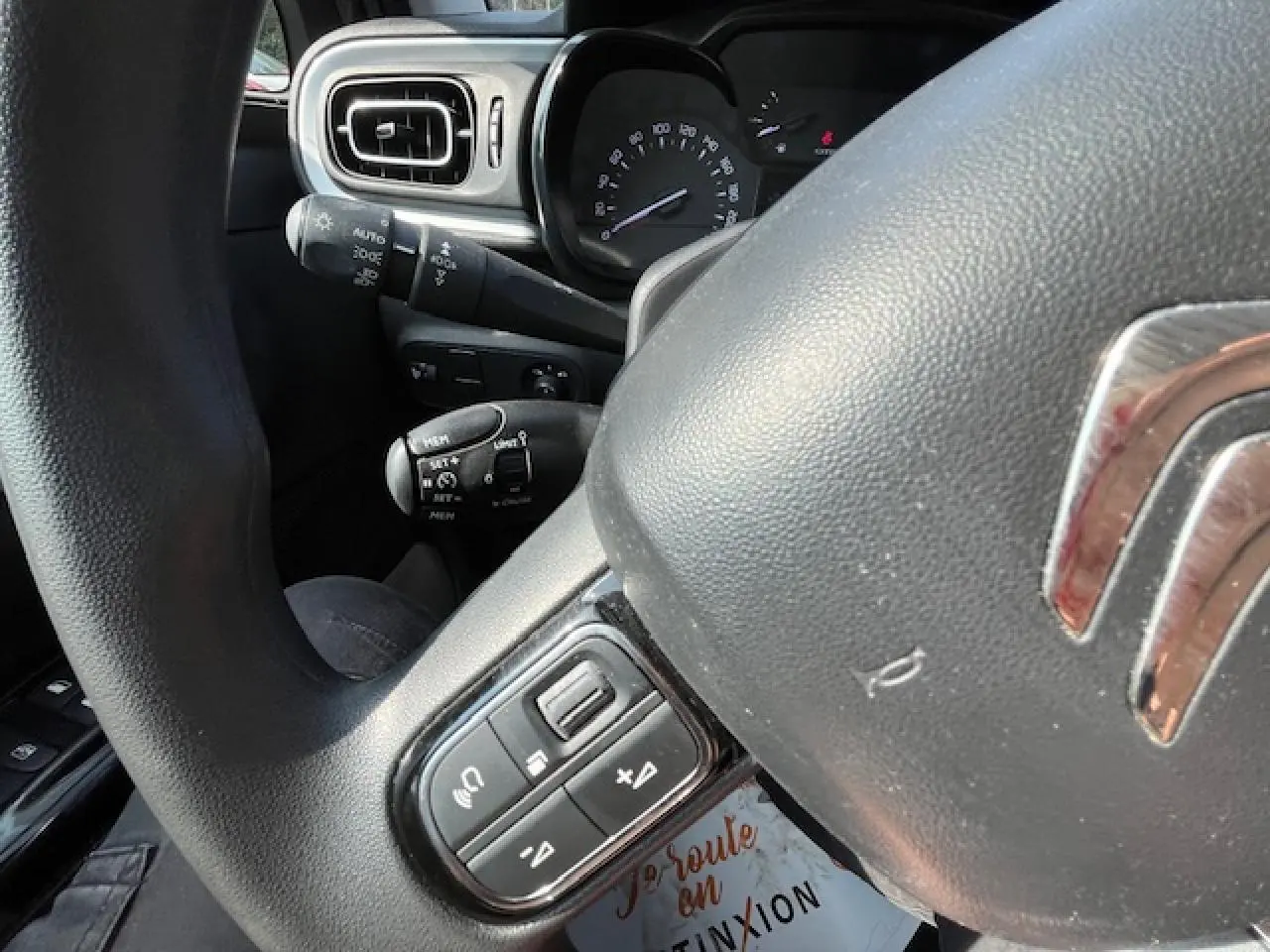 Gros plan sur le volant et le tableau de bord noir d'une Citroën C3 2023, avec commandes audio au volant visibles.