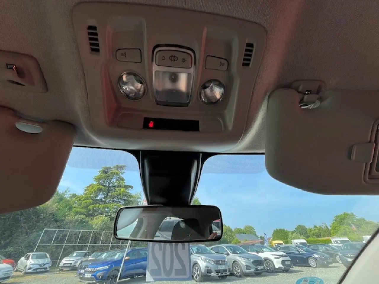 Vue intérieure du plafond et du rétroviseur central d'une Citroën C3 noire 2023, avec pare-soleil baissé et ciel dégagé visible.