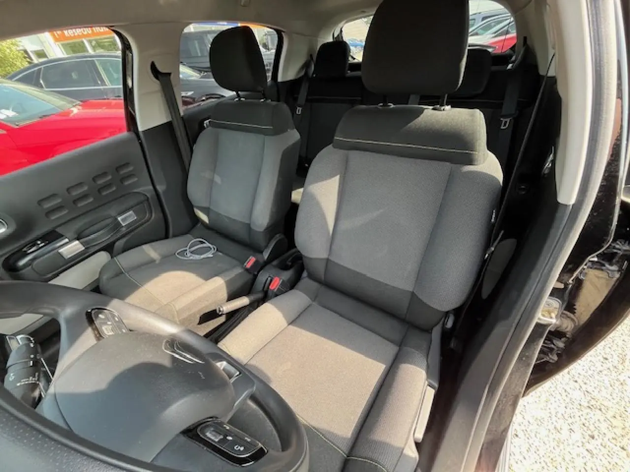 Vue intérieure côté conducteur d'une Citroën C3 noire 2023, mettant en valeur les sièges tissu gris et le volant multifonction.