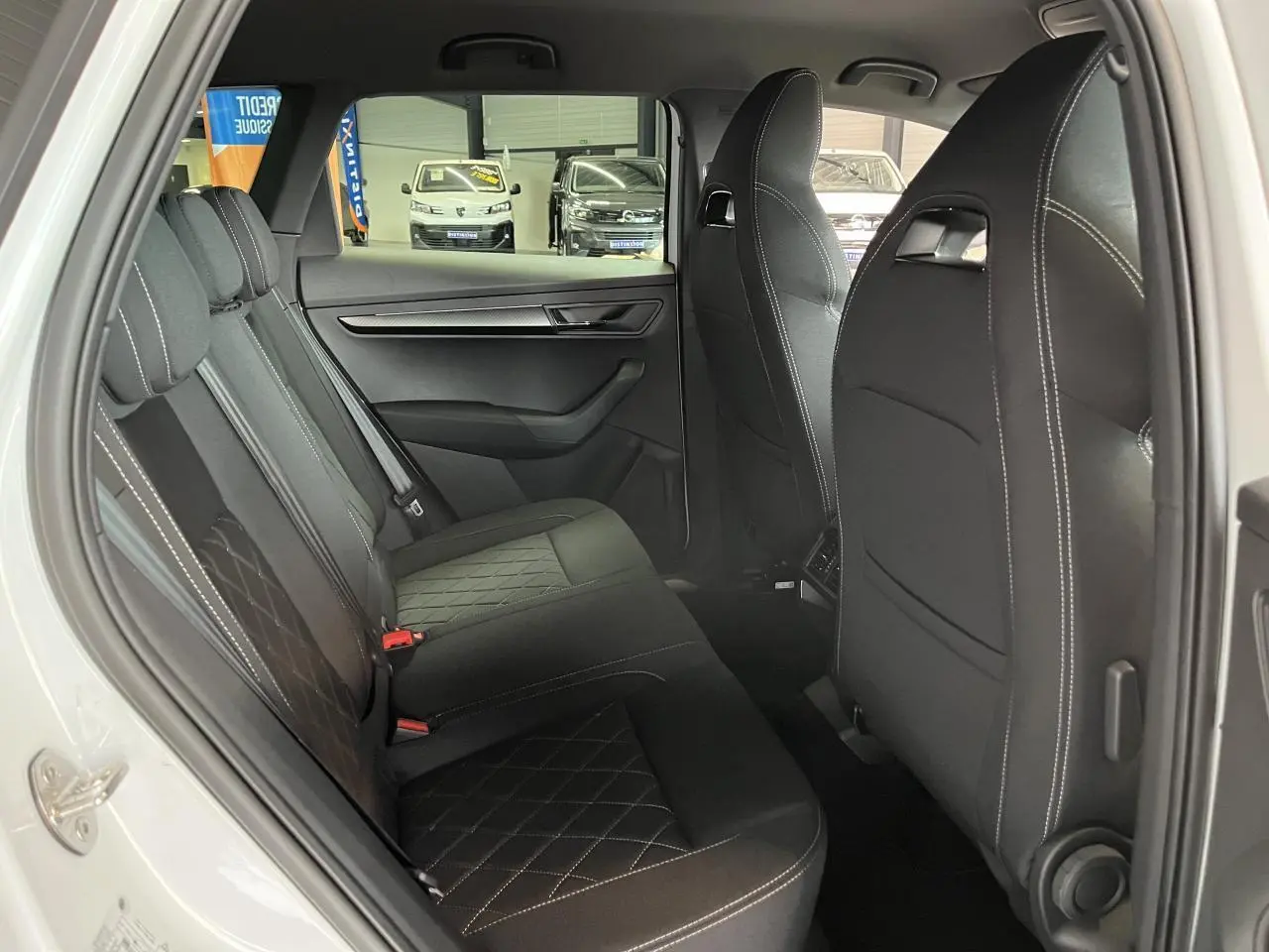 Vue côté gauche de l'intérieur arrière du SKODA KAROQ blanc avec sièges noirs et surpiqûres contrastées.