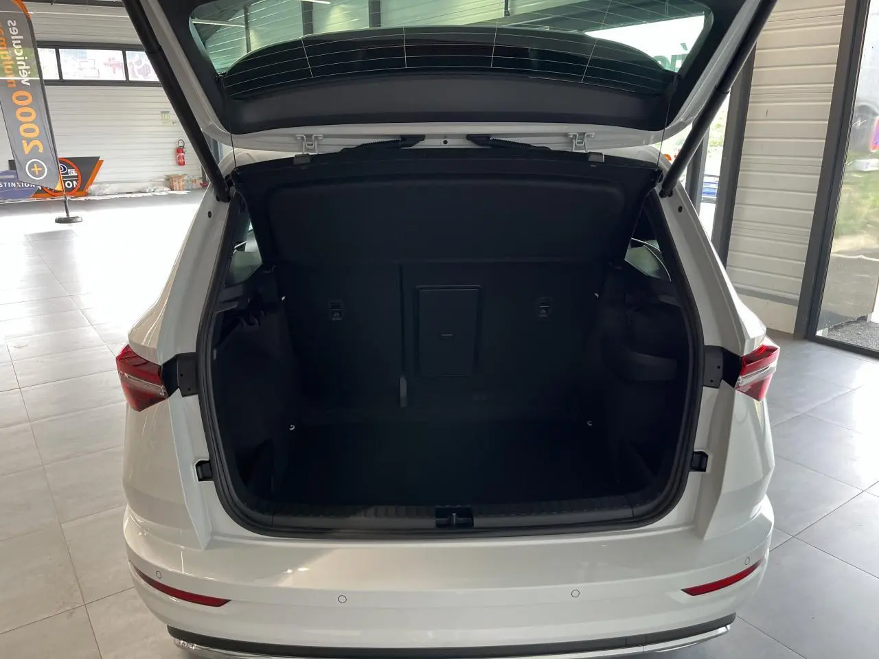 Coffre ouvert d'un SUV SKODA KAROQ blanc 2025 vu de l'arrière, montrant l'espace de chargement intérieur noir.