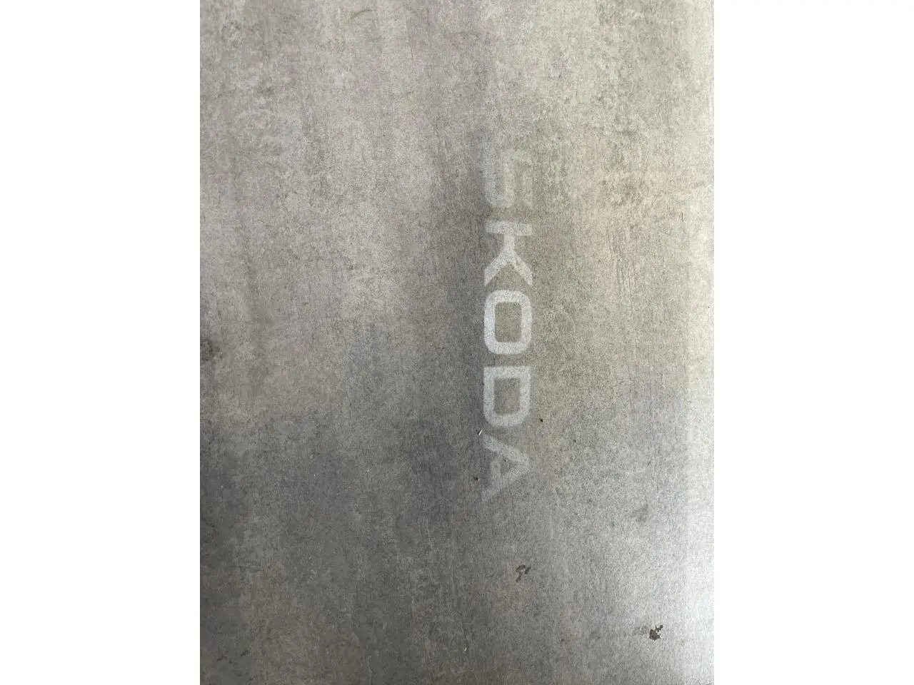 Projection lumineuse du logo SKODA au sol, visible à côté d'un véhicule blanc, angle latéral droit.