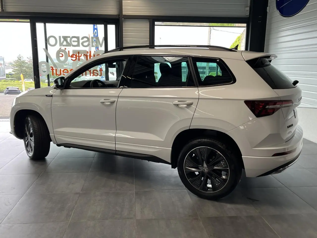 Vue latérale droite du SUV blanc SKODA KAROQ 1.5 TSI Sportline avec jantes alliage noires et vitres teintées.
