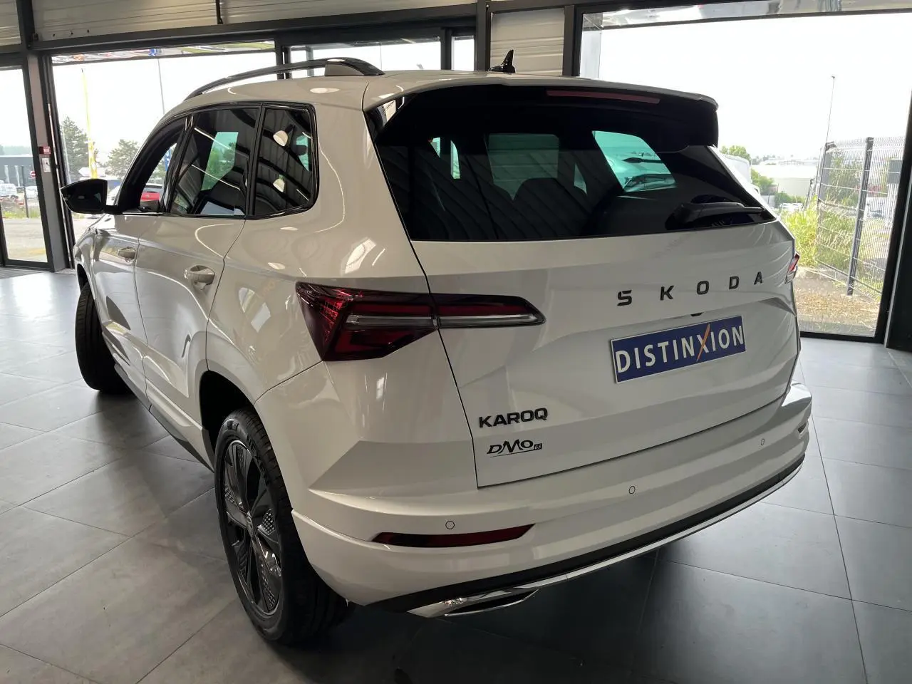 Vue 3/4 arrière droite du SUV blanc SKODA KAROQ 2025 avec jantes anthracite et hayon électrique en intérieur showroom.