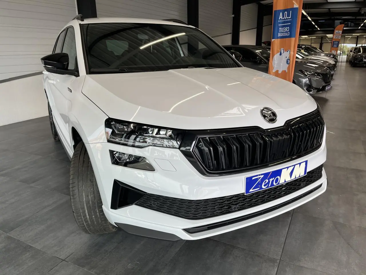 SUV SKODA KAROQ blanc en 3/4 avant droit avec calandre noire et phares LED dans un showroom.