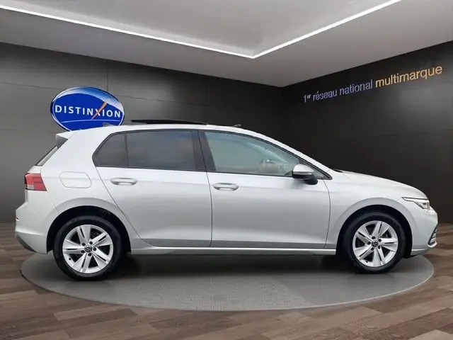 Profil côté gauche d'une Volkswagen Golf VIII gris argent avec vitres surteintées et toit panoramique ouvrant dans un showroom.