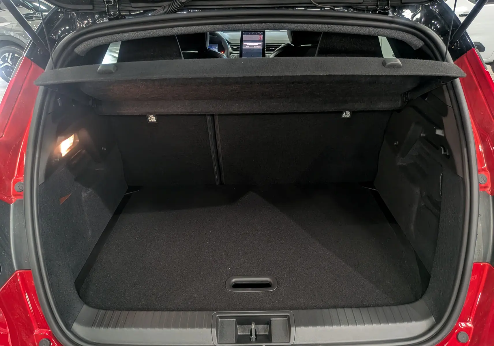 Coffre ouvert vu de l'arrière du Renault Captur E-TECH rouge Flamme avec toit noir, montrant un espace de chargement vide et lumineux.