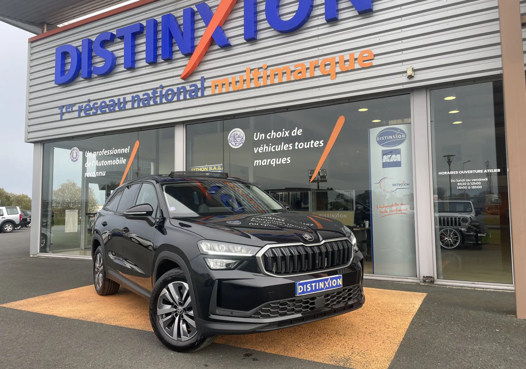 SUV Skoda Kodiaq noir métal vu en 3/4 avant droit devant un showroom Distinxion avec calandre marquée.