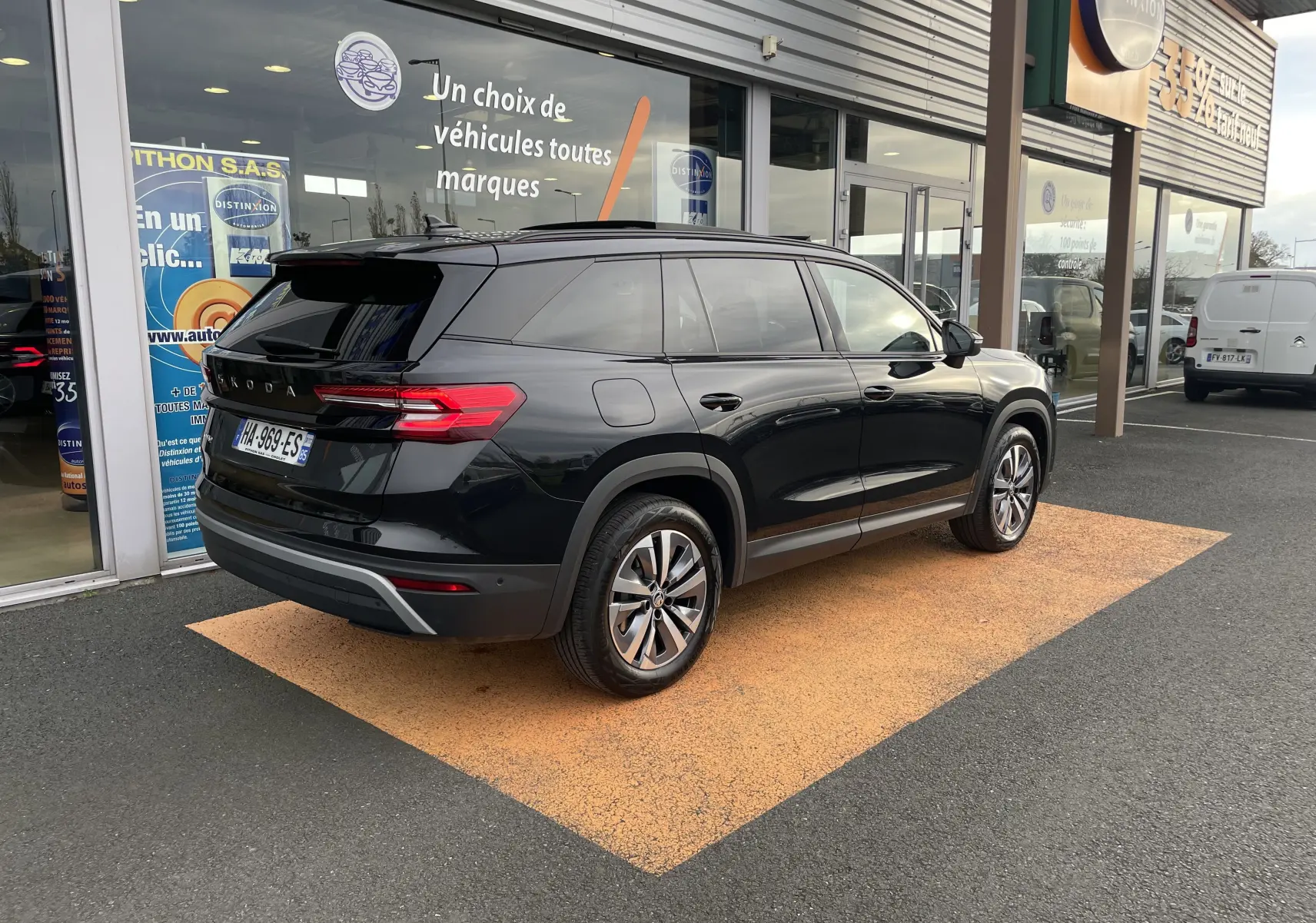 Vue 3/4 arrière droite d'un Skoda Kodiaq noir métal 2024 garé devant un showroom avec vitres teintées et jantes alliage.