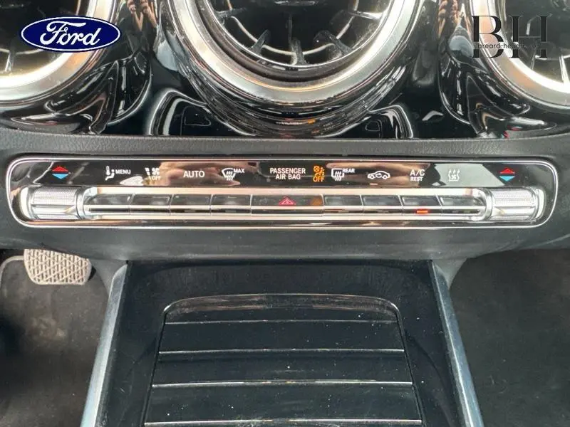 Tableau de bord noir brillant avec commandes climatisation et ventilation d'une Mercedes GLA 250 e bleu denim vue de face.