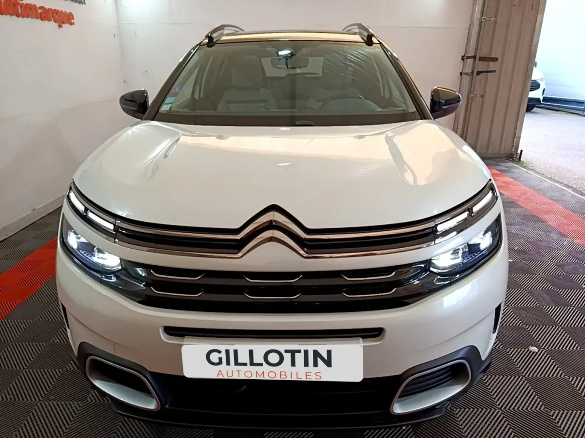 Vue avant d'un Citroën C5 Aircross Hybrid blanc avec phares LED allumés dans un showroom.