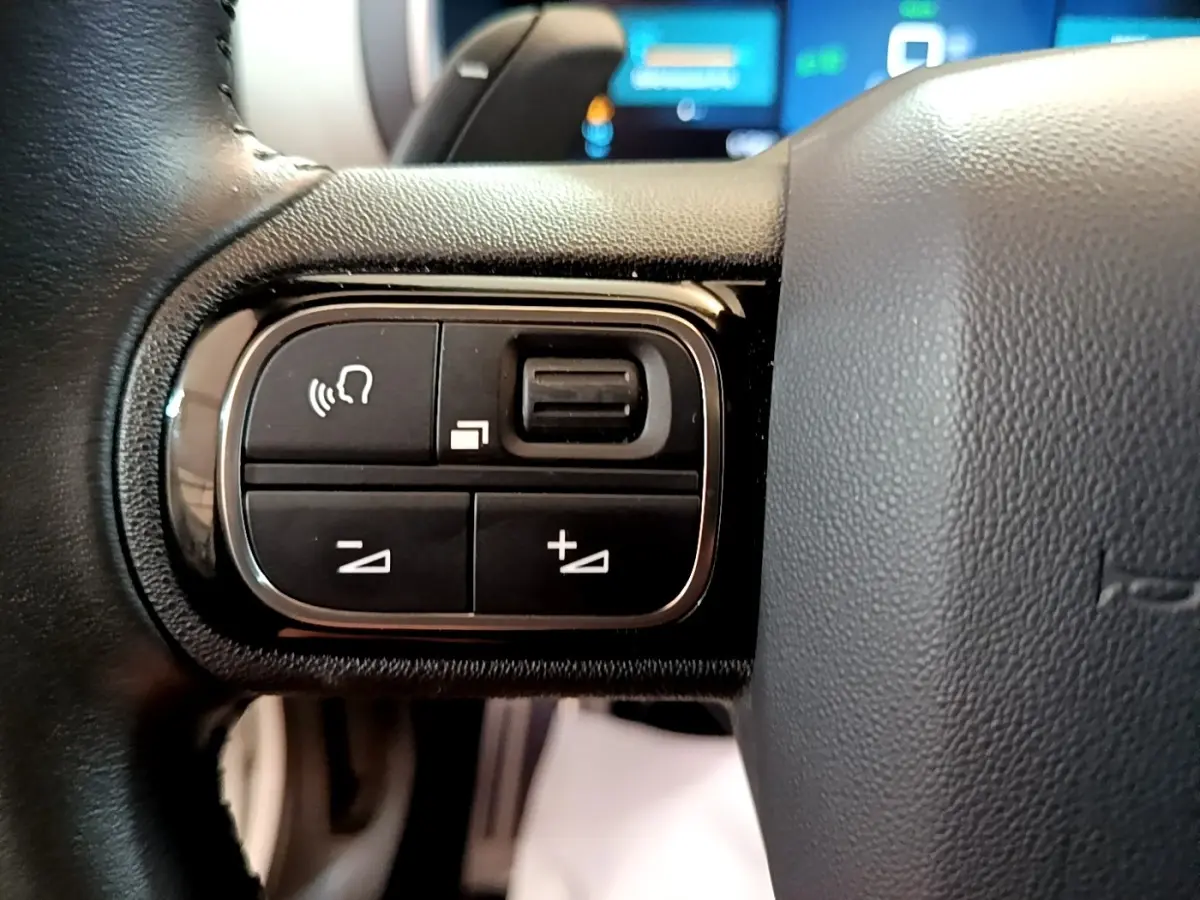 Gros plan sur les commandes gauche du volant cuir du Citroën C5 Aircross Hybrid blanc, boutons multifonctions visibles.