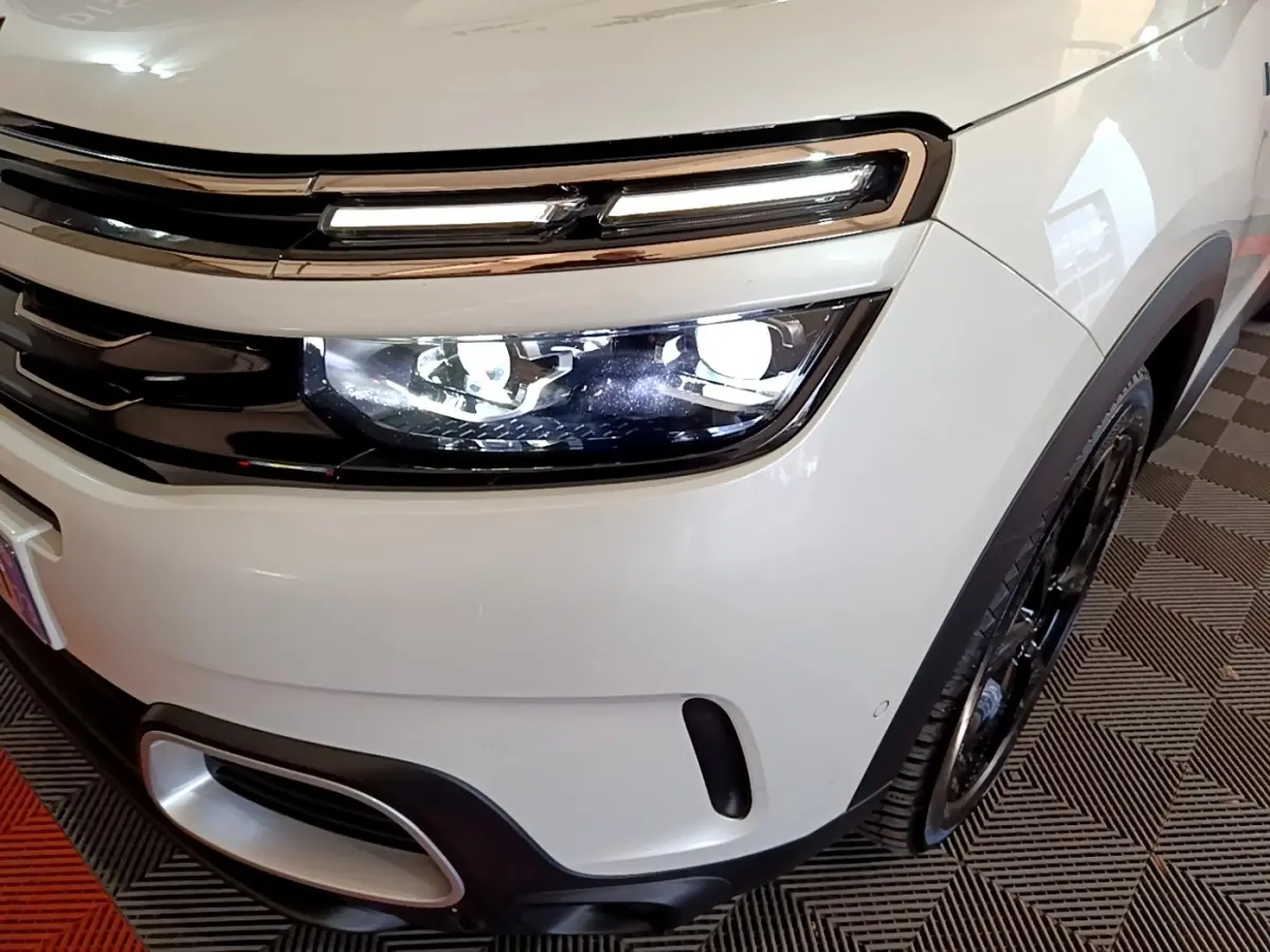 Gros plan sur l'avant droit blanc du Citroën C5 Aircross Hybrid avec phares LED allumés et jante noire visible.