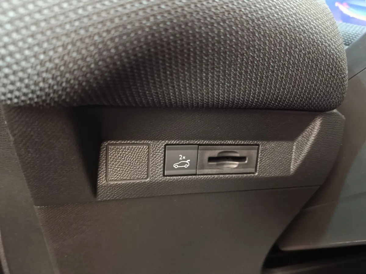 Gros plan sur le bouton d'ouverture du coffre noir, situé sous le siège d'une Citroën C5 hybride verte.