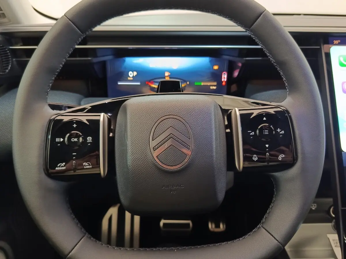 Vue rapprochée du volant noir de la Citroën C5 hybride 2026 avec commandes intégrées et logo central argenté.