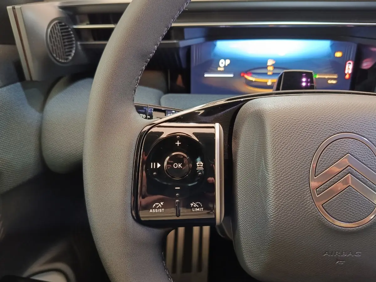 Gros plan sur le volant gris de la Citroën C5 Hybride avec commandes multifonctions et combiné digital lumineux en arrière-plan.