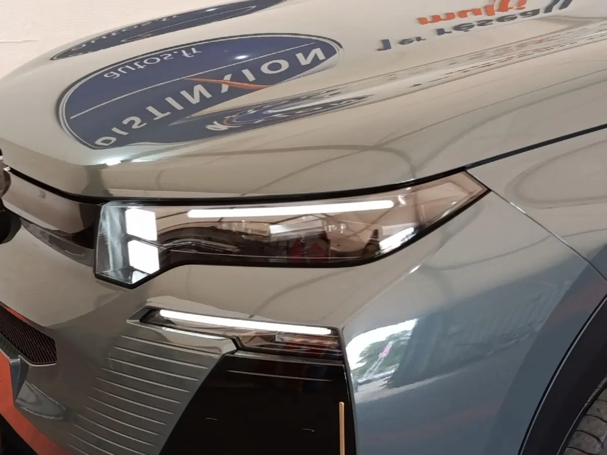Gros plan sur le phare avant droit du Citroën C5 hybride vert 2026 avec détails lumineux modernes et carrosserie brillante.