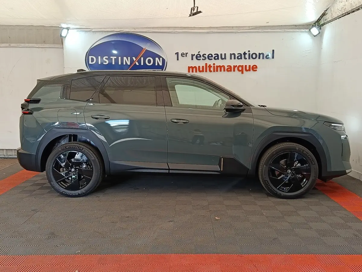 Vue latérale droite d'un Citroën C5 Hybride 145ch vert avec jantes noires et vitres teintées en intérieur showroom.