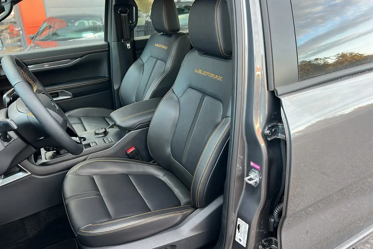 Vue intérieure côté conducteur du Ford Ranger 3.0 V6 240 Wildtrak Plus 2025 en gris carbone, sièges cuir noirs avec surpiqûres jaunes Wildtrak.