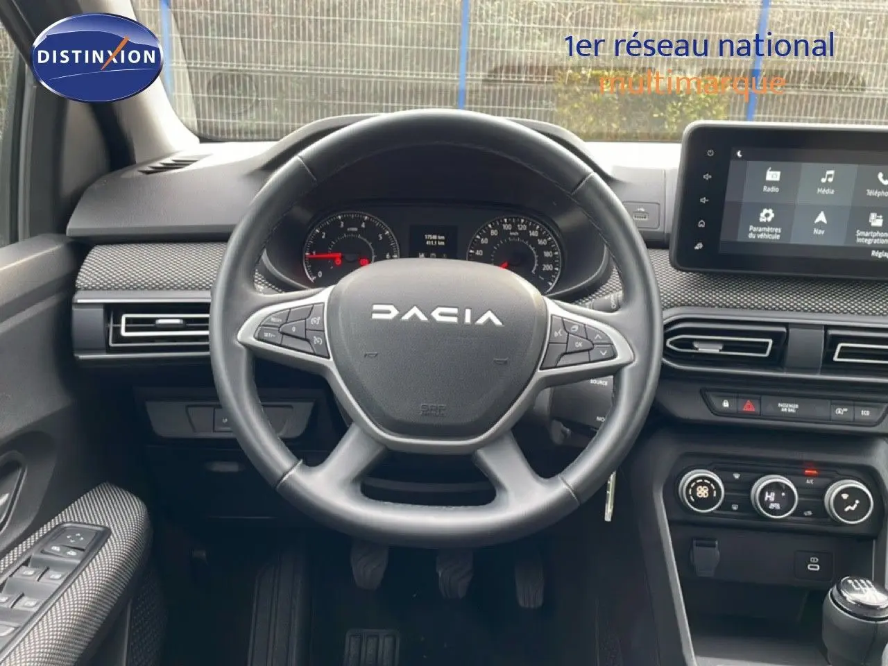 Vue intérieure centrée sur le volant DACIA d'un Jogger 2025, avec tableau de bord et écran tactile en arrière-plan.