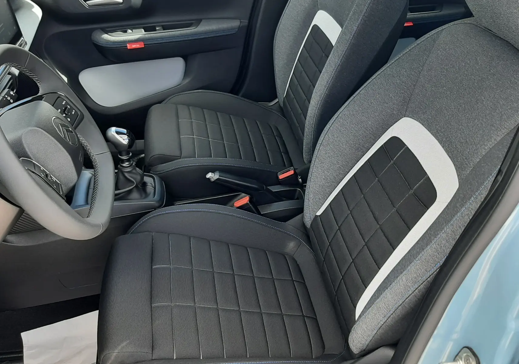 Vue intérieure côté conducteur de la Citroën C3 Turbo 100ch Plus 2026, sièges tissu noir et gris, volant et levier de vitesse visibles.