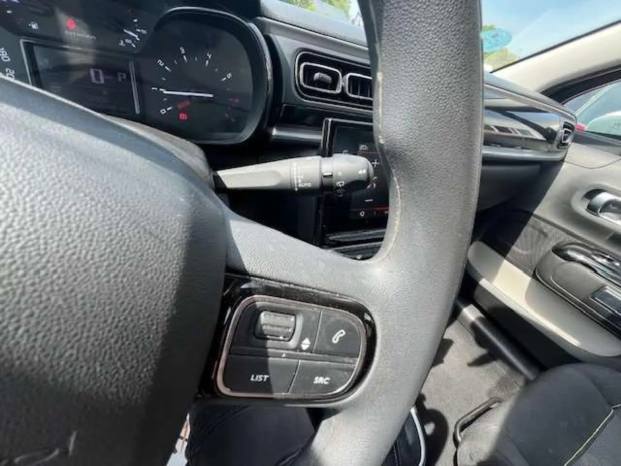 Vue rapprochée du volant noir de la Citroën C3 2023, avec commandes audio et tableau de bord en arrière-plan.