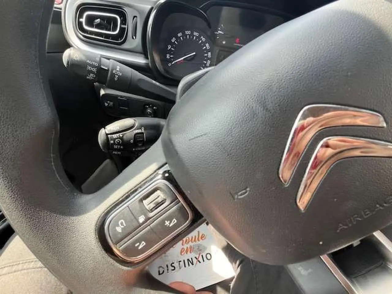 Gros plan sur le volant noir de la Citroën C3 2023 avec commandes audio intégrées et logo chromé visible.