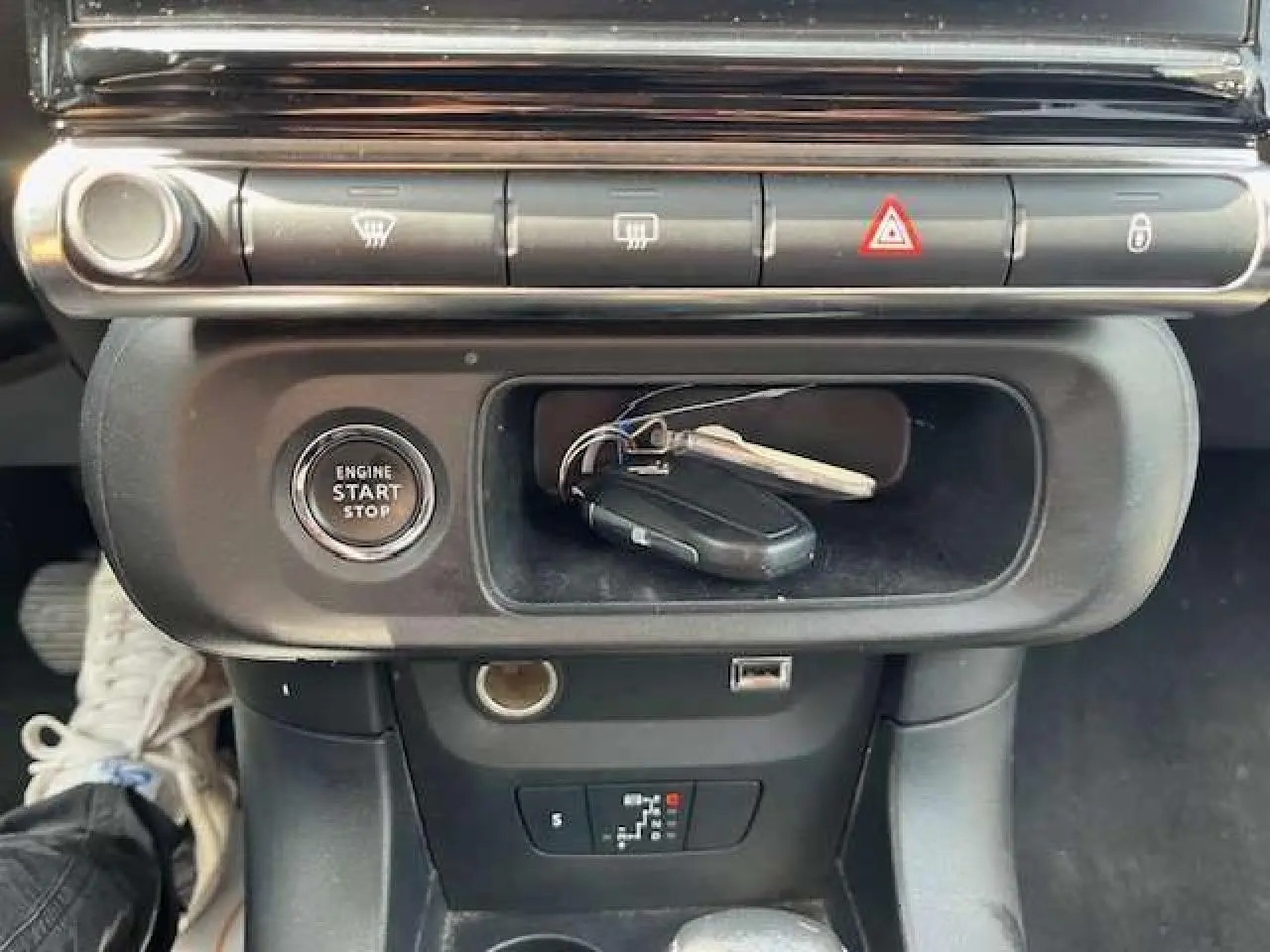 Vue rapprochée de la console centrale de la Citroën C3 2023 avec bouton start/stop et clés posées dans le rangement noir.
