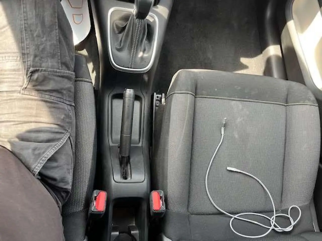 Vue plongeante sur la console centrale et les sièges avant noirs de la Citroën C3 2023, câble USB posé sur le siège passager.