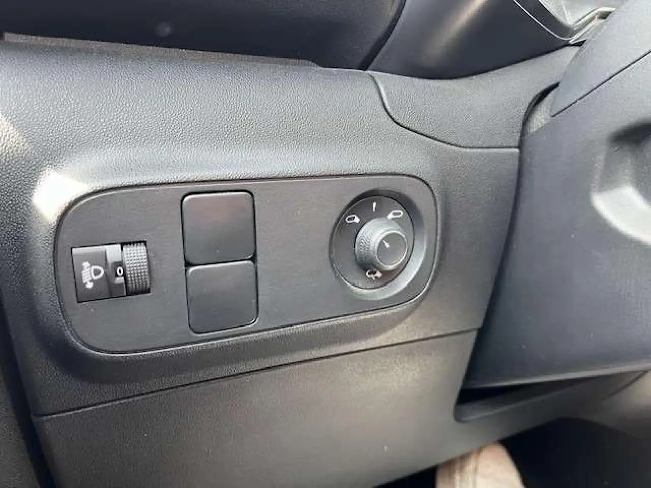 Gros plan sur les commandes de réglage des rétroviseurs et des phares dans l'habitacle noir du Citroën C3 2023.