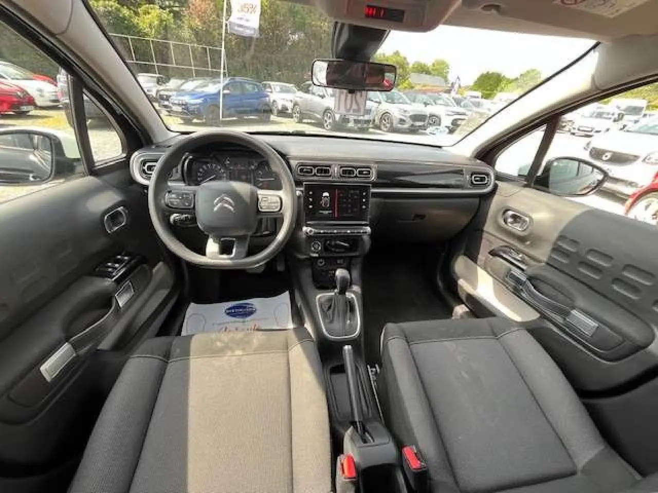 Intérieur de la Citroën C3 2023 vu de face, avec tableau de bord noir et sièges tissu gris foncé.