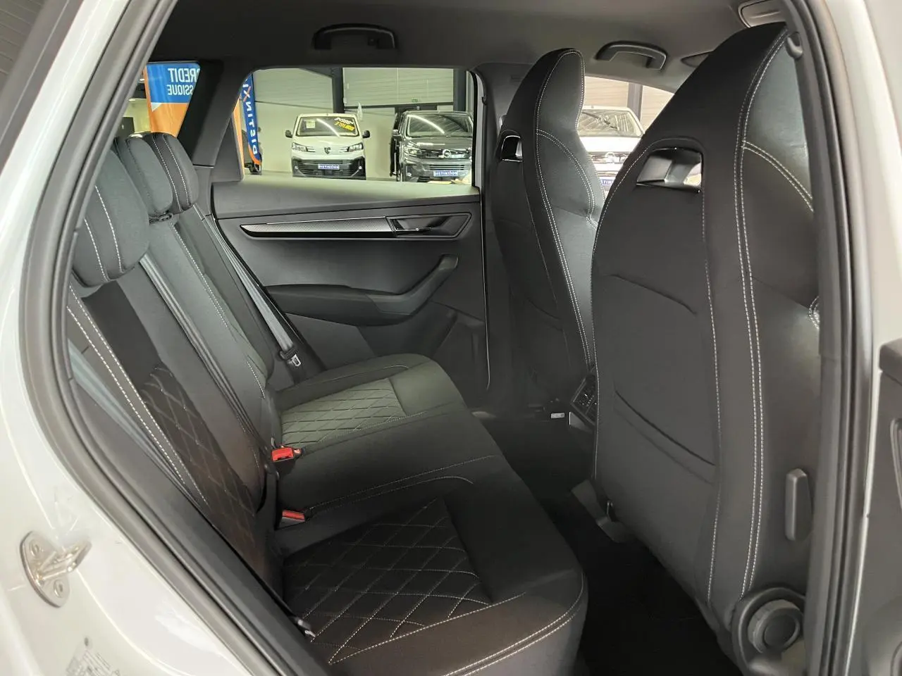 Vue côté gauche sur l'intérieur arrière noir avec surpiqûres blanches du Skoda Karoq blanc 2025 Sportline
