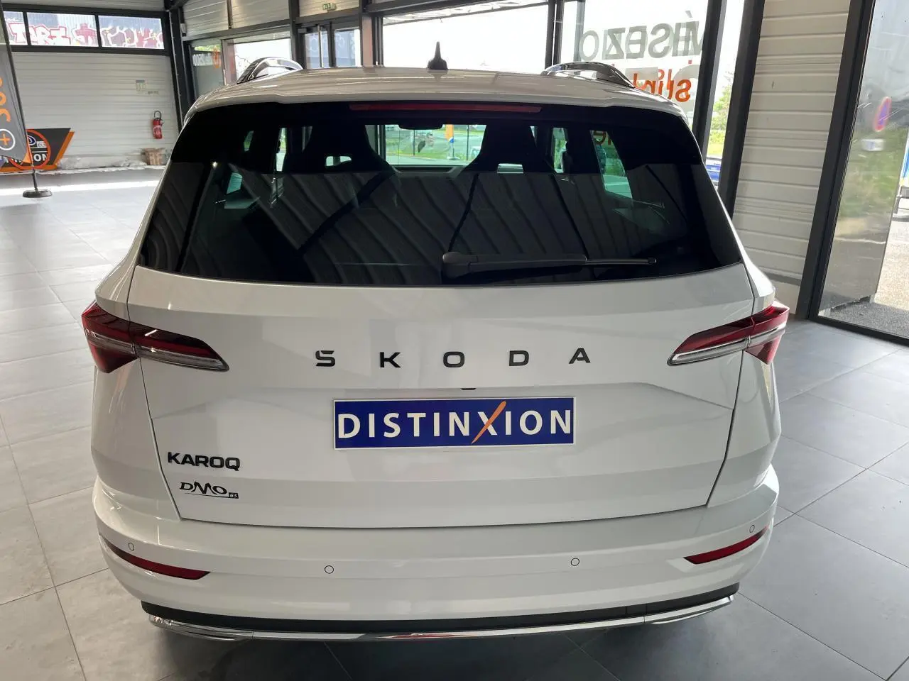 Vue arrière d'un SUV SKODA KAROQ blanc 2025 avec hayon électrique et feux arrière LED en intérieur showroom.