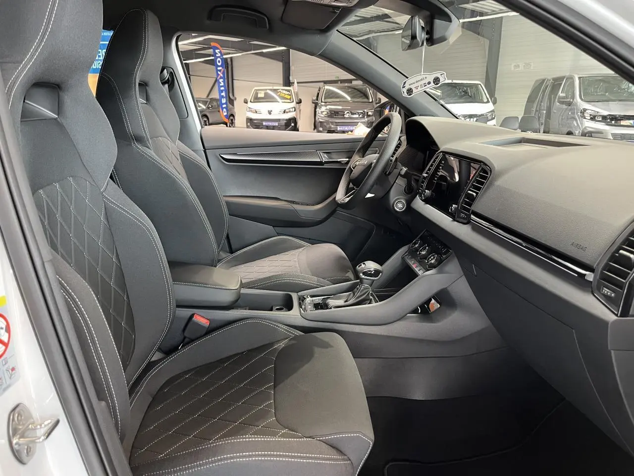 Intérieur du SKODA KAROQ 1.5 TSI blanc, vue côté conducteur, sièges sport noirs avec surpiqûres blanches et tableau de bord moderne.