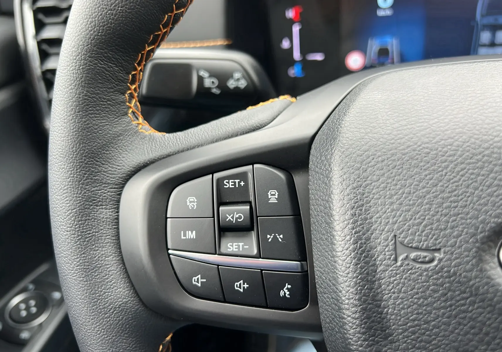 Gros plan sur les commandes au volant du Ford Ranger 2025 gris carbone, version Wildtrak Plus avec surpiqûres orange.
