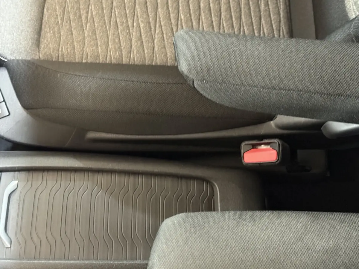 Vue intérieure rapprochée du siège conducteur et de la console centrale avec tissu gris et ceinture de sécurité rouge.