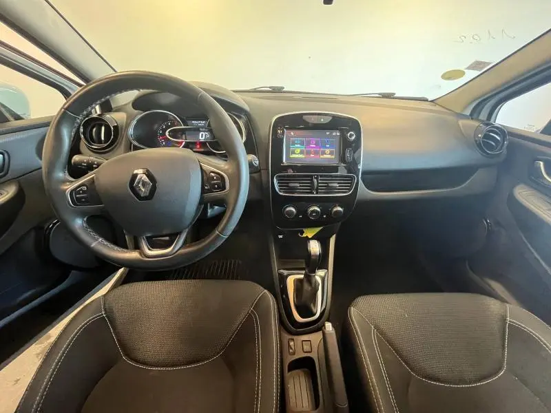 Vue intérieure avant du tableau de bord et volant cuir noir de la Renault Clio Estate 1.5 dCi blanche de 2019 avec écran tactile central.